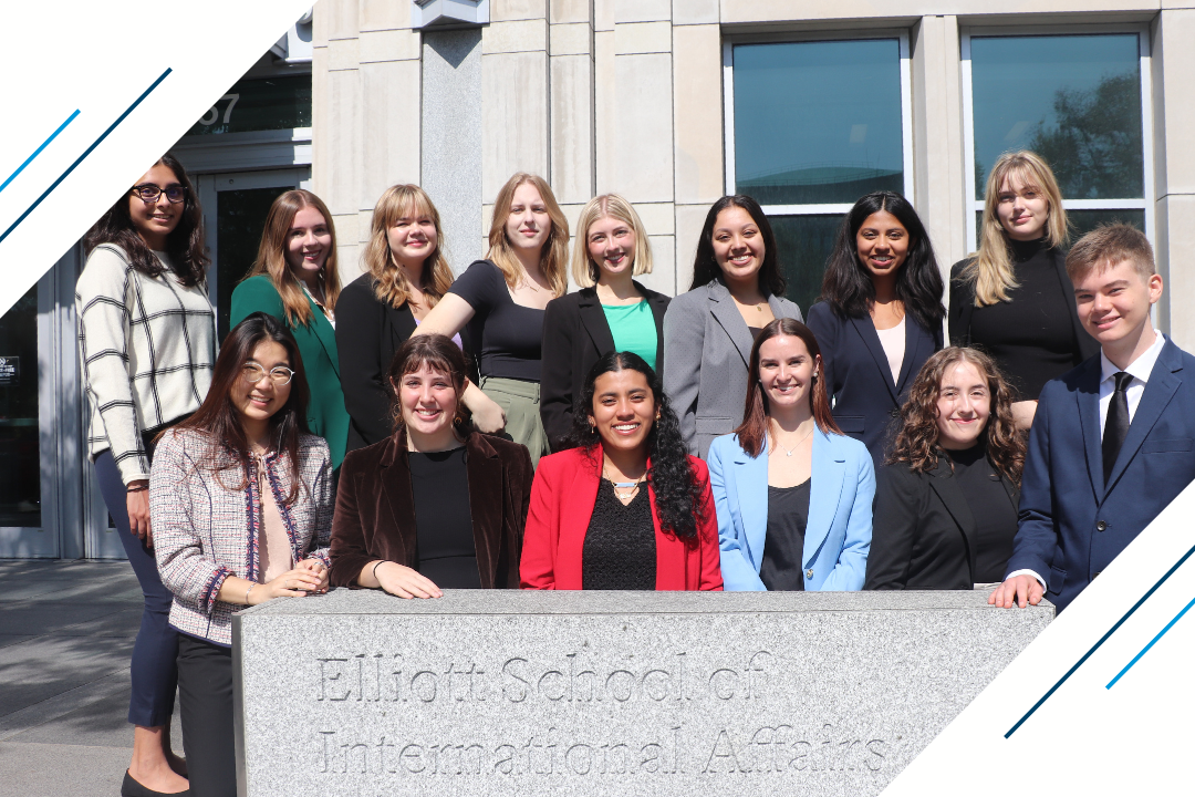 All the Deans Scholars standing together outside at the front the Elliott School, surrounding the schools sign that reads "Elliott School of International Affairs"