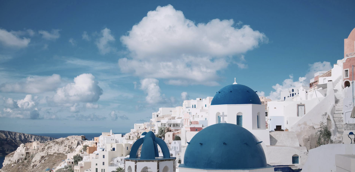 Greek island landscape: whitewashed building with blue domes under blue sky.