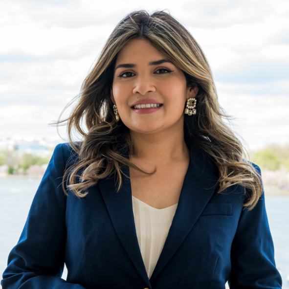 Javeria Ali smiles. She is wearing a blue blazer and standing in front of the tidal basin in DC