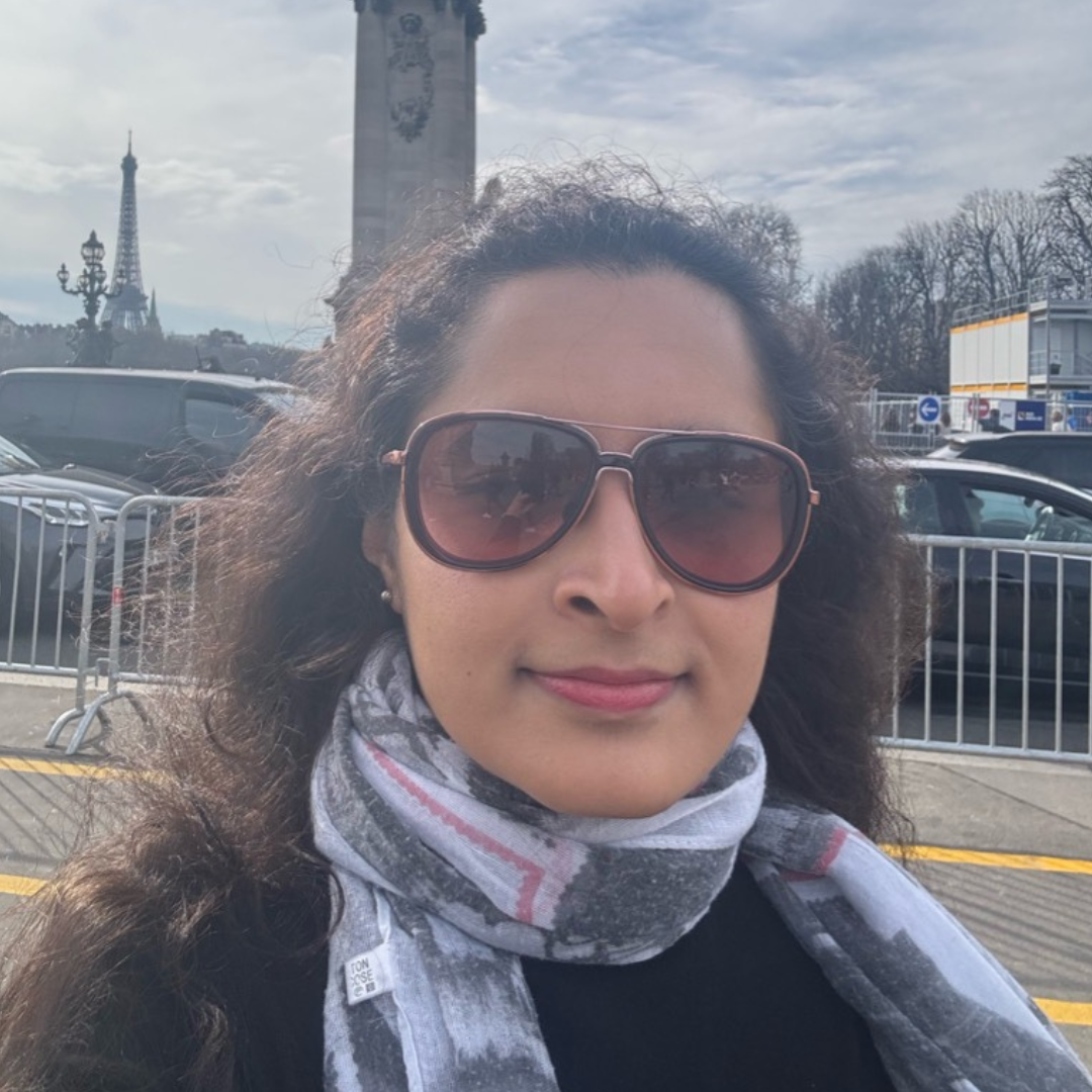 Sapna Suresh smiles, outside in a city wearing a grey scarf