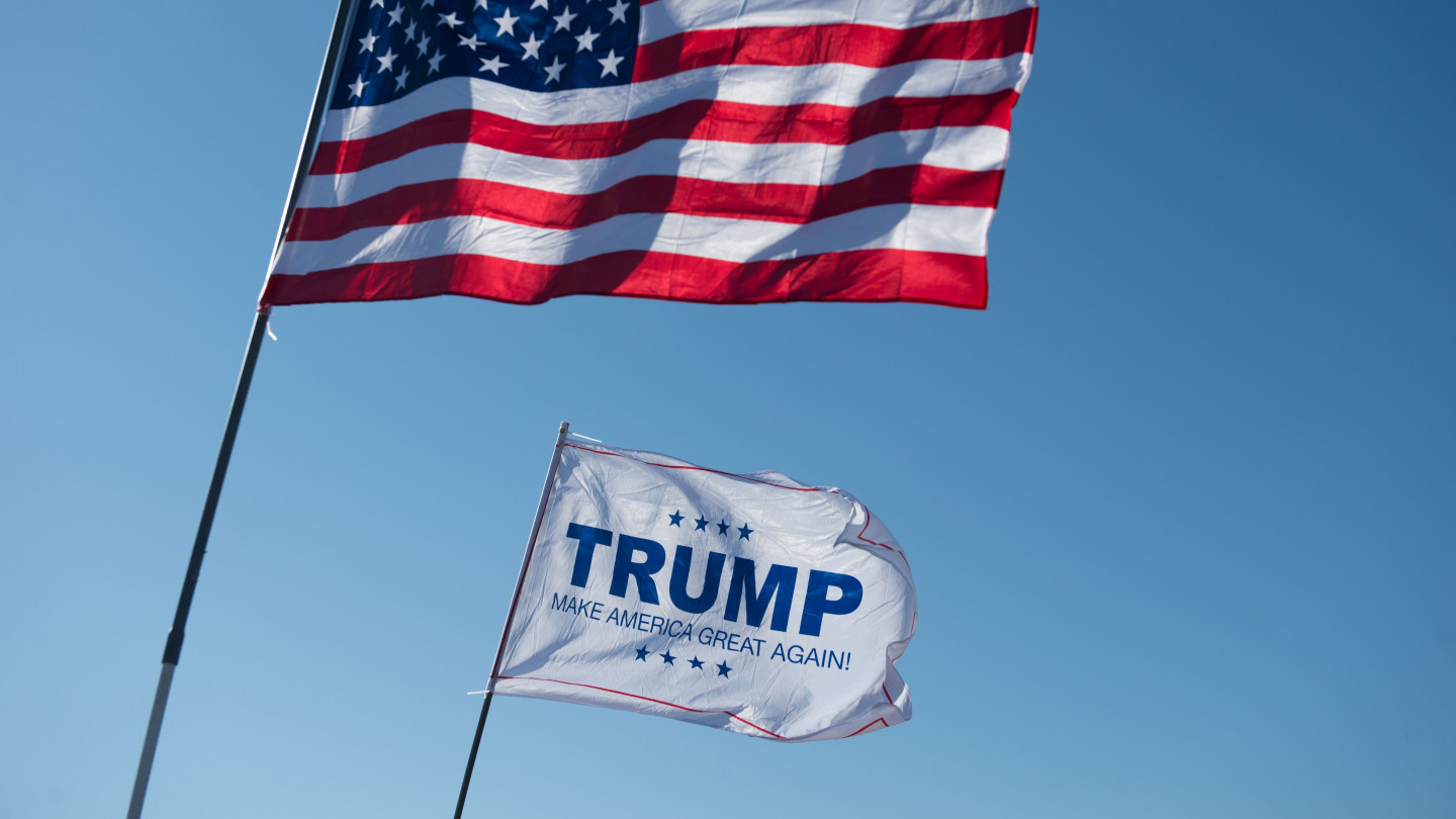 An American flag and Trump flag waving next to each other.