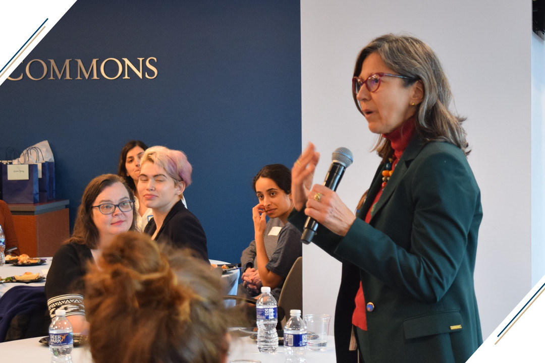 a woman stands and speaks to the audience at an Global Gender Policy event with students and other guests listening in the background