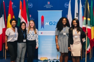 photo: five students stand in front of the Model G20 Summit logo and flags