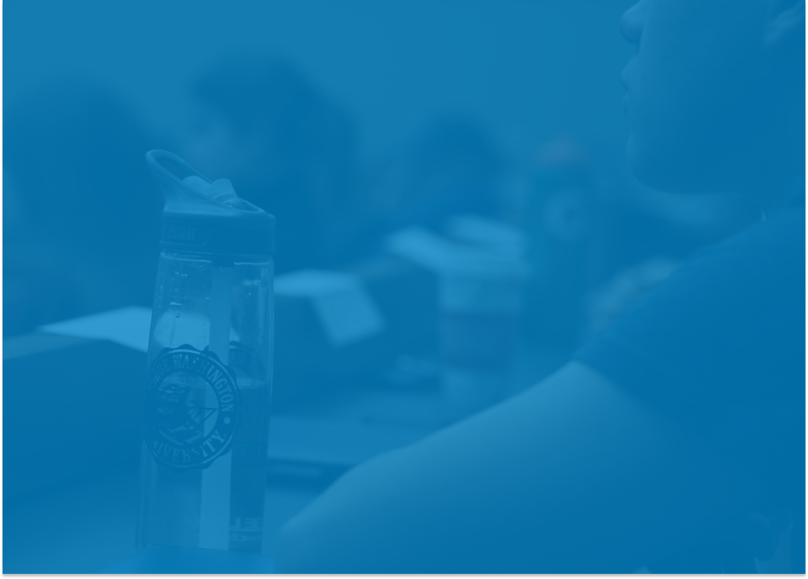 Close up shot of a male student looking to the front of a lecture hall with his water bottle to his left. 