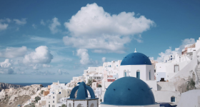 Greek island landscape: whitewashed building with blue domes under blue sky.