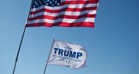 An American flag and Trump flag waving next to each other.